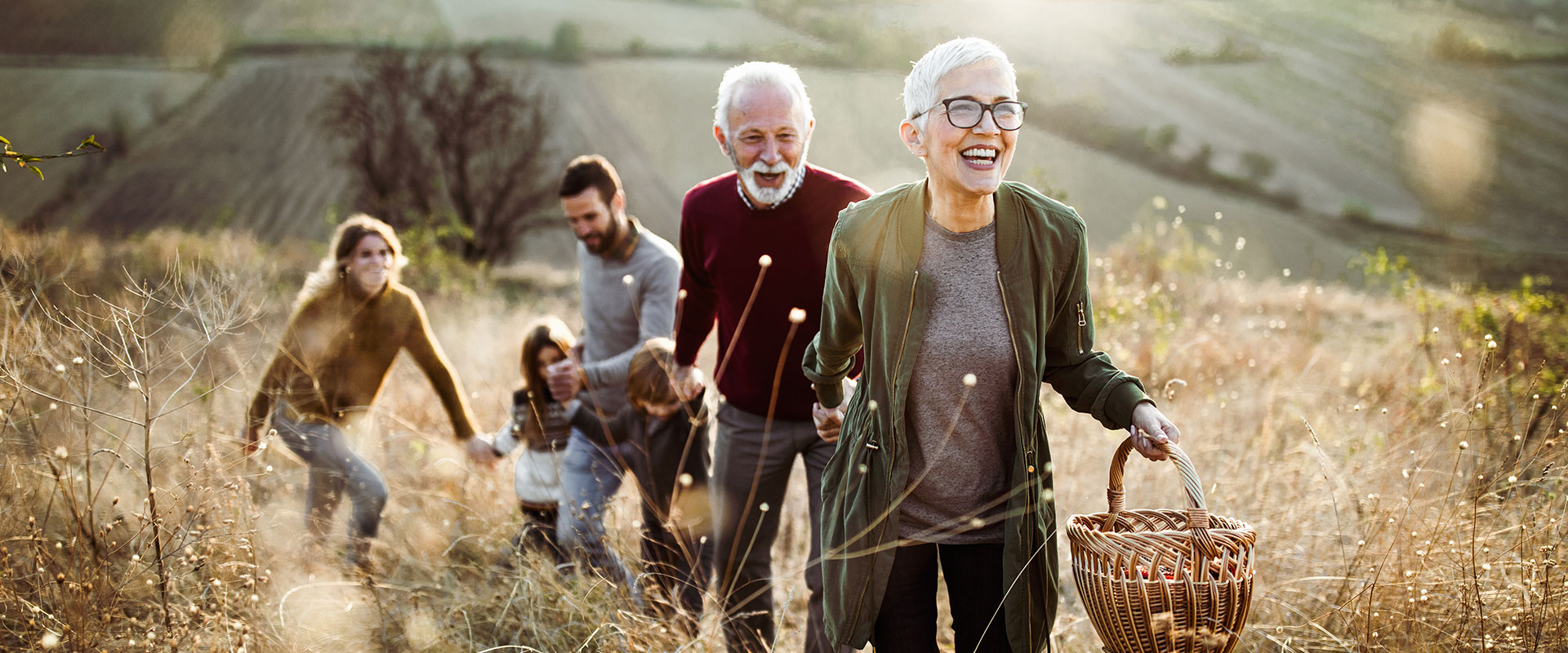 Happy senior woman leading her family to perfect picnic place on the hill.