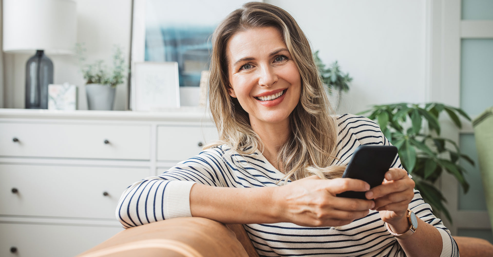 Mature woman at home relaxing on sofa. She is using smart phone.