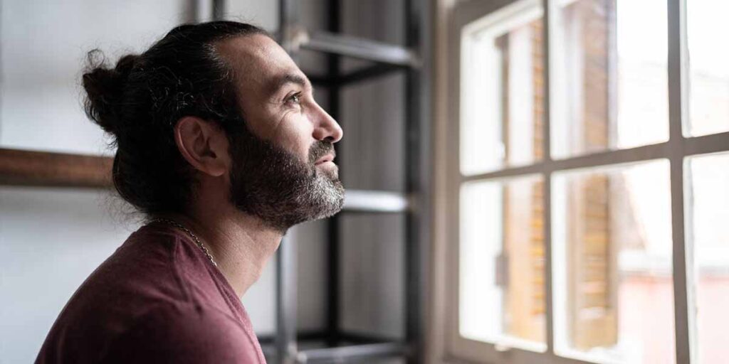 man looks out window with expression of gratitude