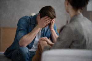 Psychologist talking with patient on therapy session. Depressed man speaking to a therapist while she is taking notes