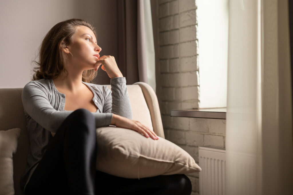 Portrait of lonely sad young woman sitting near window of apartments.